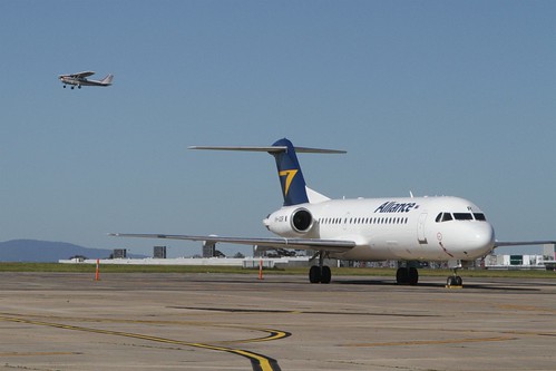 Light plane passes over parked Alliance Airlines Fokker F70 VH-QQR