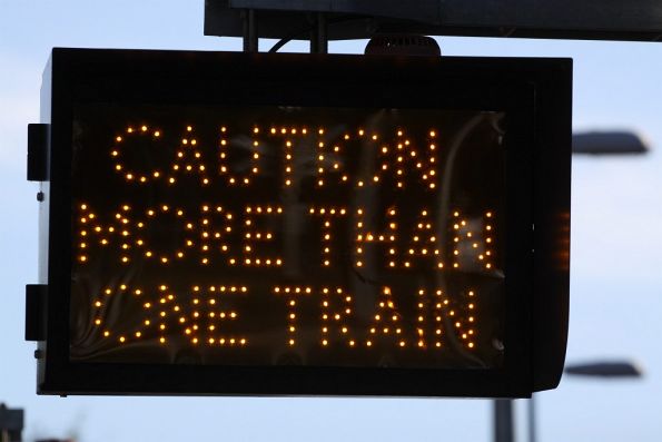 Illuminated 'Caution more than one train' warning sign at a crib crossing