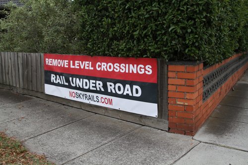 'Remove Level Crossings / Rail Under Road / NoSkyrails.com' poster on a house backing onto the railway at Carnegie