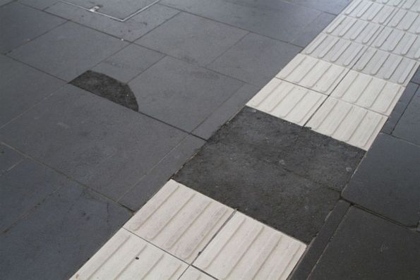 Broken bluestone slabs and tactile paving at the main entrance from Spencer Street, patched up with asphalt