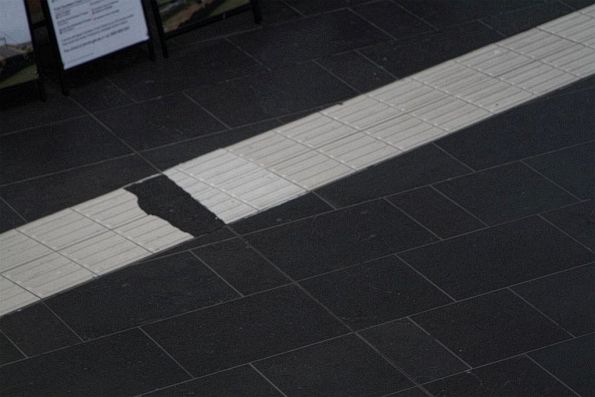 Broken tactile paving on the V/Line concourse, patched up with asphalt